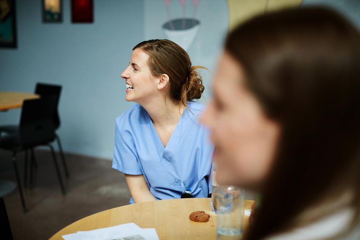 Smiling female medical workers looking away while sitting at table in hospital cafeteria