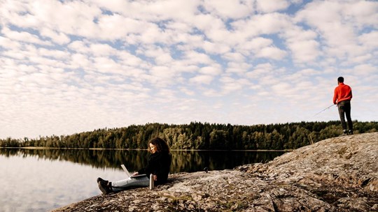 Woman working on laptop while man fishing