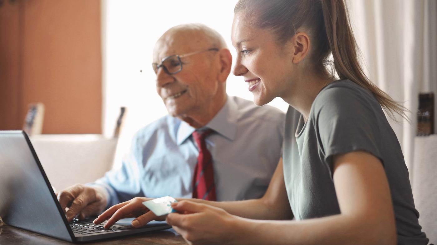 Young woman helping granddad with online banking on a laptop