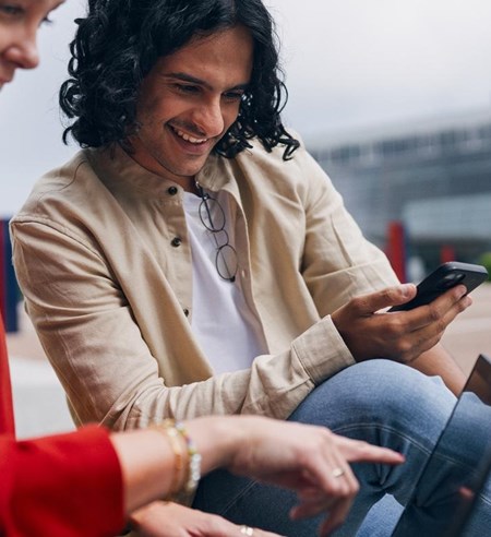 Man and woman working on laptop using cell phone smiling next to Tietoevry office building